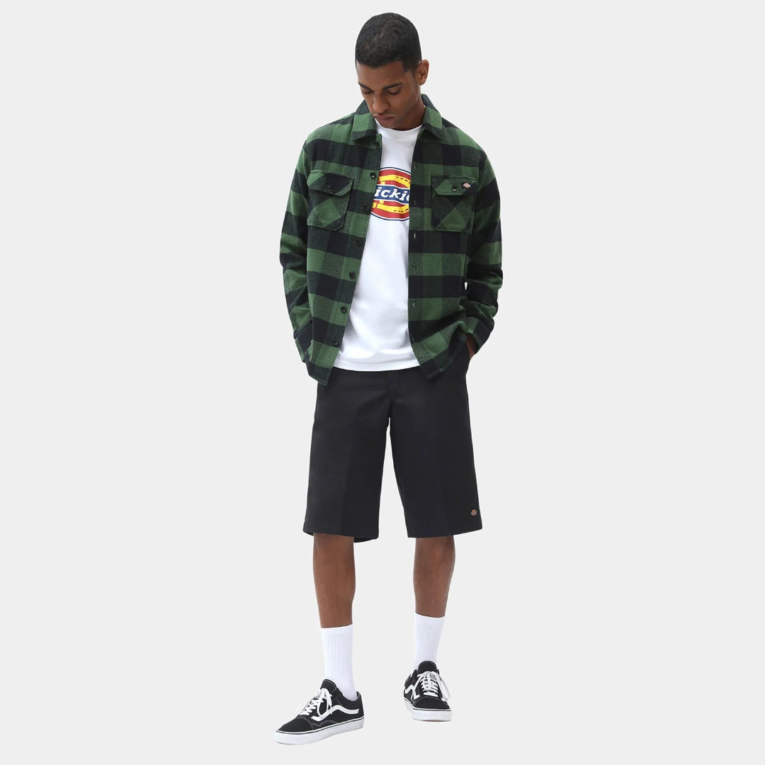 Person wearing a green plaid shirt, white t-shirt with colorful design, black shorts, and black sneakers on a white background.