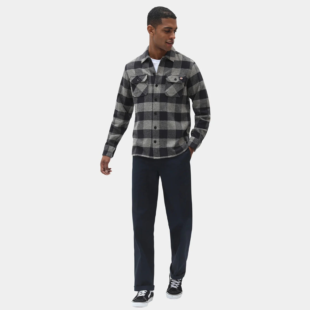 Man wearing a black and gray plaid shirt with dark pants on a white background