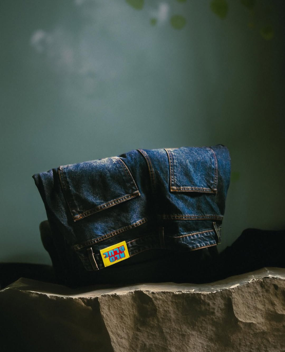 Blue denim jeans with a colorful patch on a stone surface against a green background