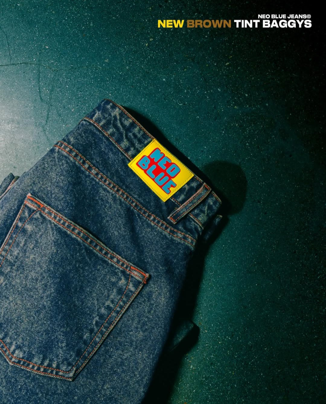 Folded blue jeans with a brand label on a dark green background
