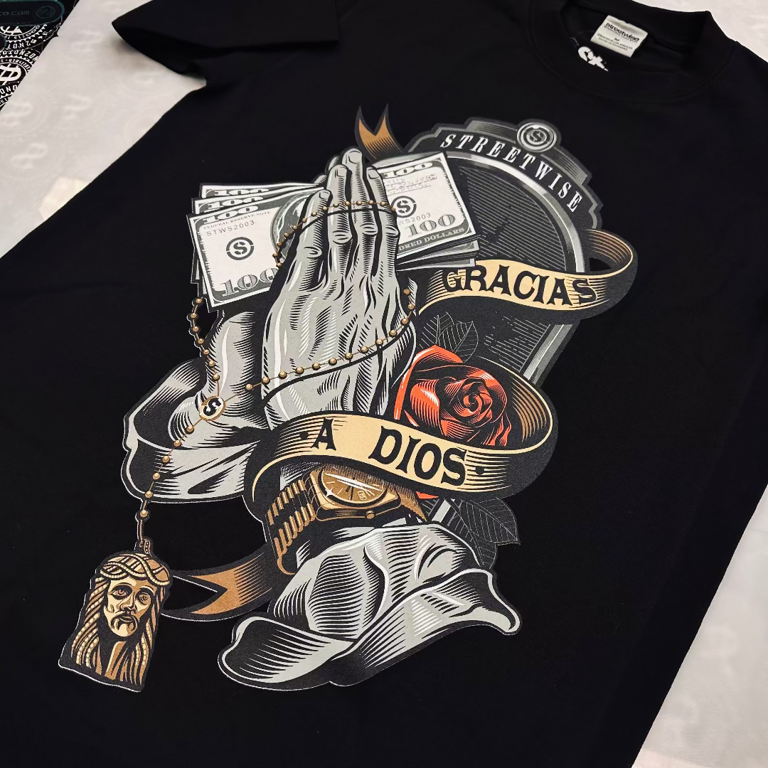 Black t-shirt with graphic design of praying hands, money, and religious symbols on a white background.