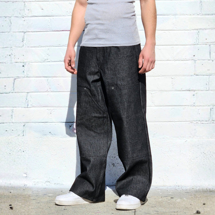 Person wearing a gray tank top and dark pants against a white brick wall.