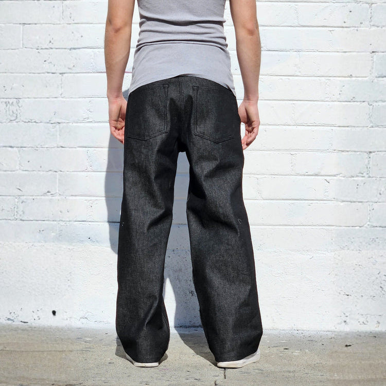 Person wearing a gray tank top and black pants standing against a white brick wall.